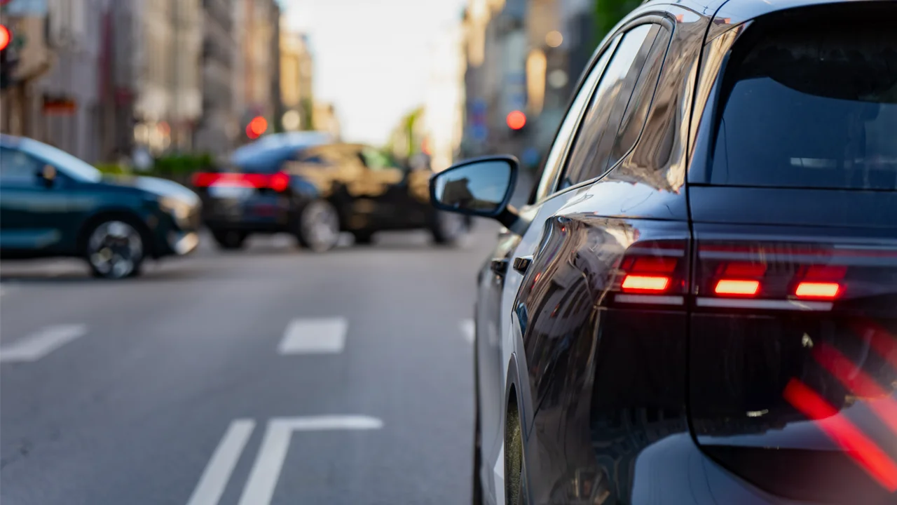 Modern black sedan driving on an open road beneath a bright sky