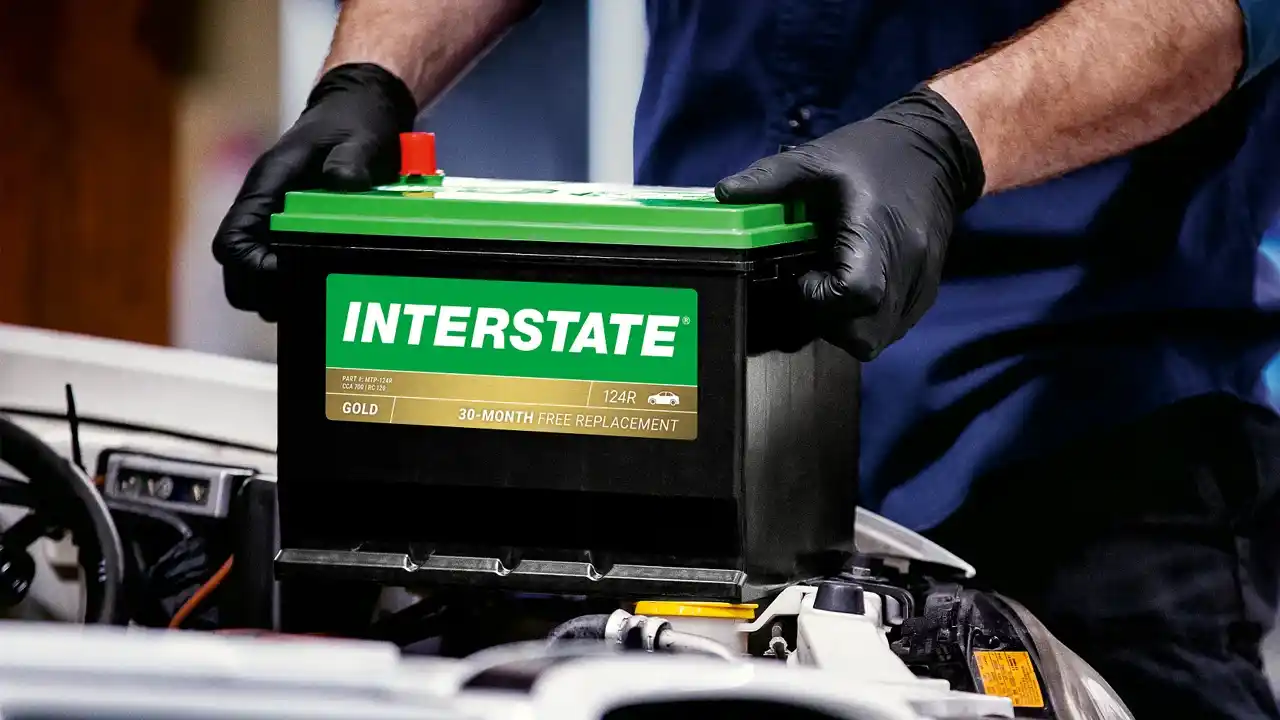Tech installing an Interstate battery into the hood of a car