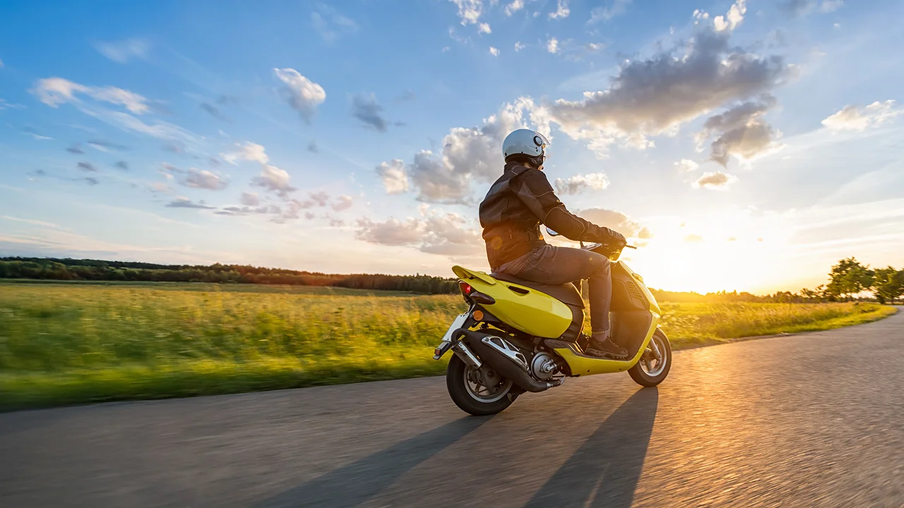 person riding scooter on the road in front of a sunset